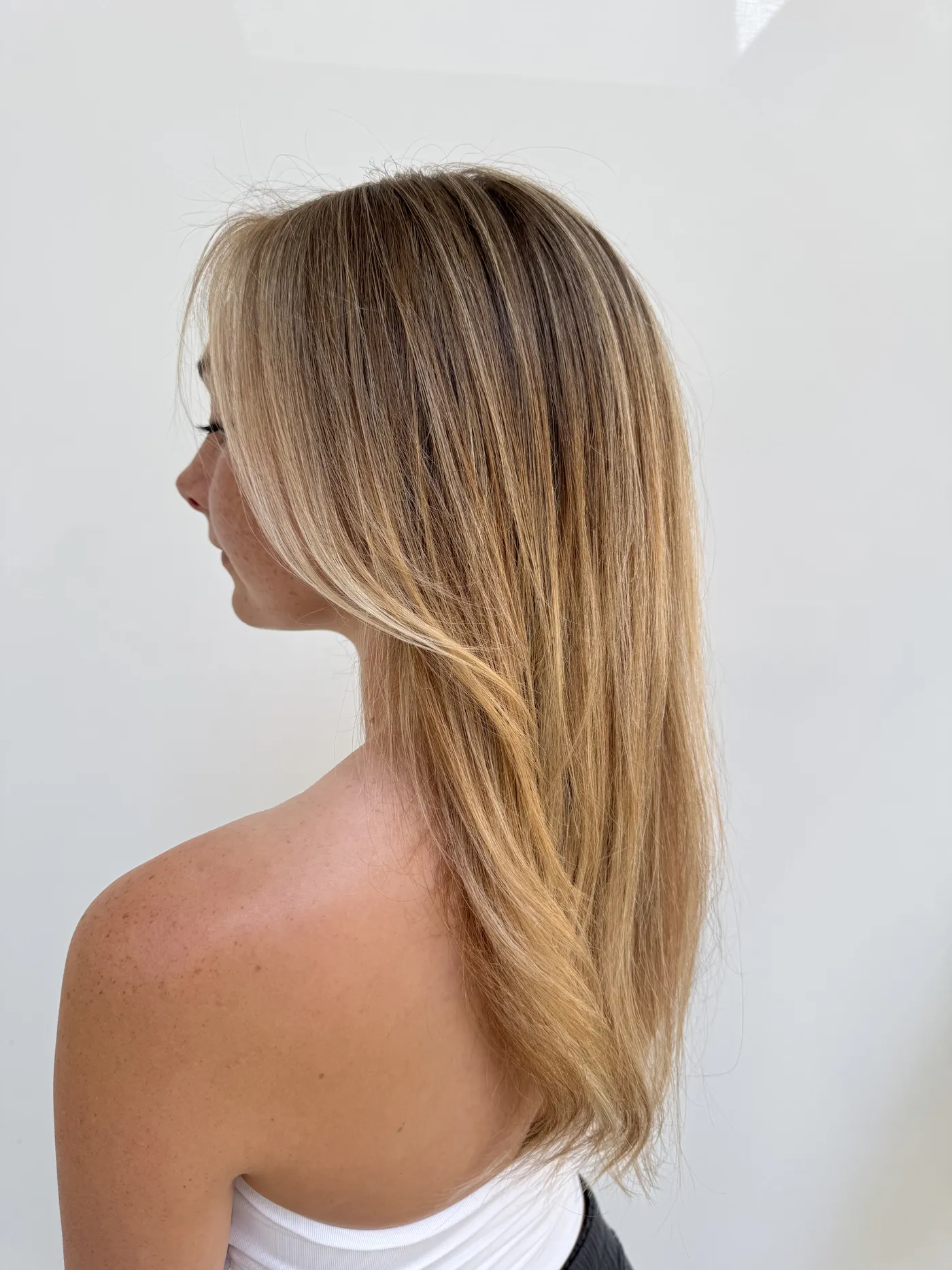 Long straight blonde hair falling over one shoulder, a soft darker root melting down into brighter, warmer ends.