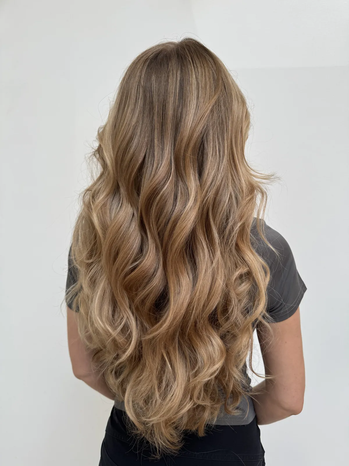 The back of long blonde hair set in loose waves, with dimensional highlights running from root to tip.